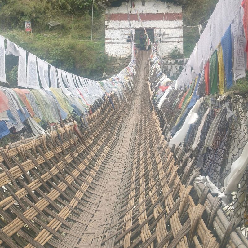 A woven cane suspension footbridge hung with prayer flags crossing a river gorge near Tawang