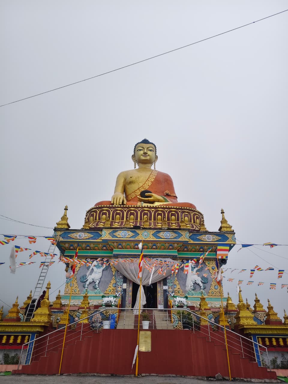 Golden Buddha statue inside Tawang Monastery, framed by prayer flags