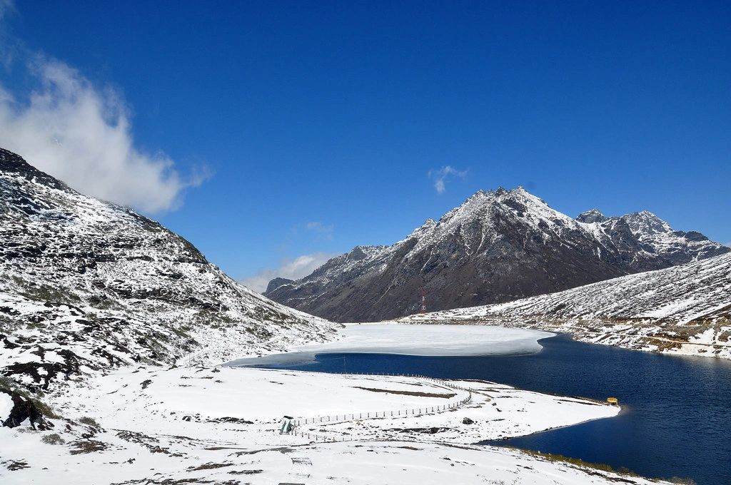 Half-frozen Sela Lake below snow-covered ridges under a clear blue winter sky