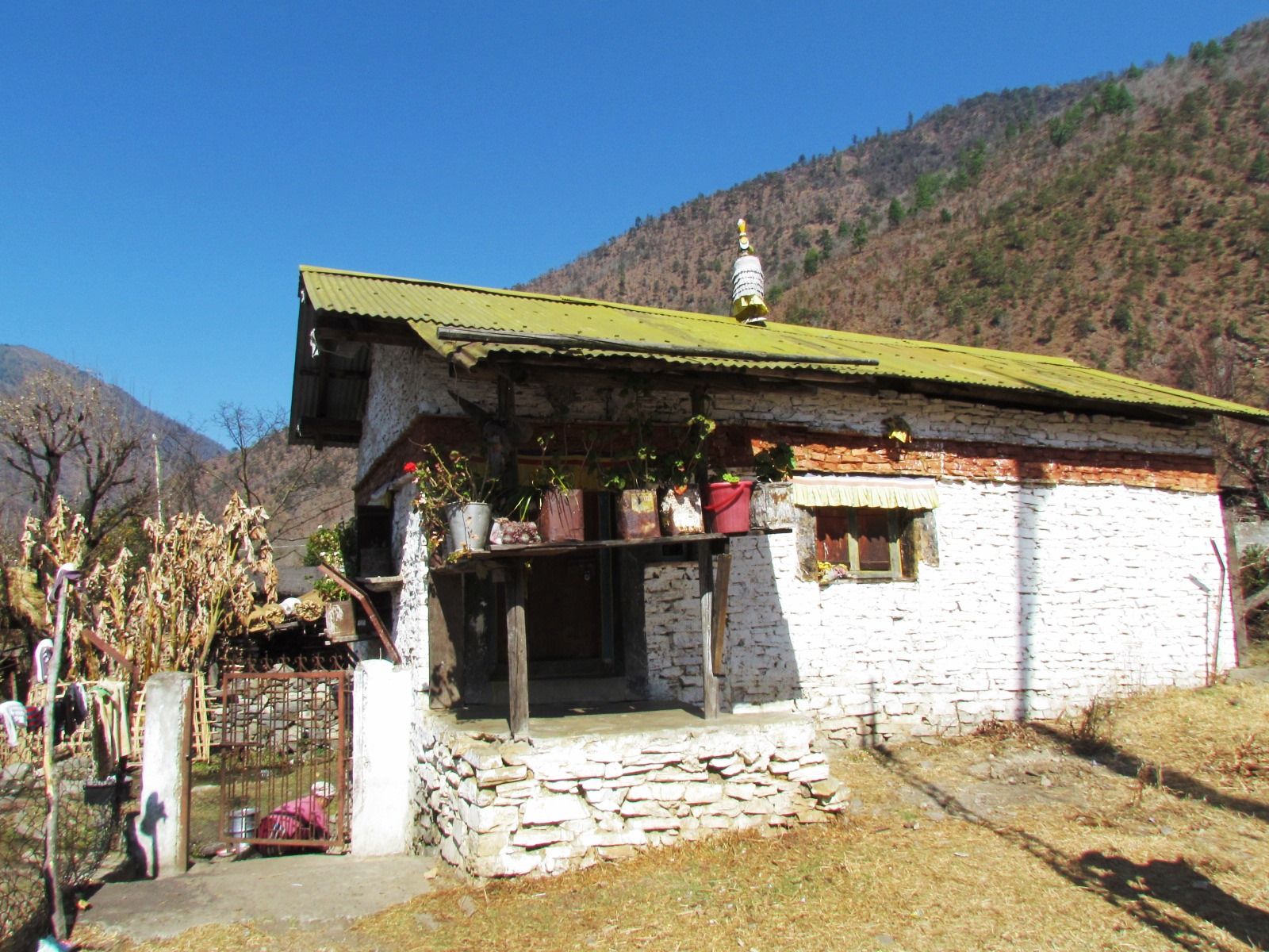 A whitewashed stone Monpa village house with a green tin roof and drying maize in West Kameng