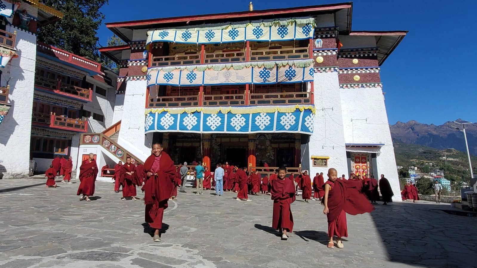 Young monks in maroon robes crossing the flagstone courtyard of Tawang Monastery after morning prayers